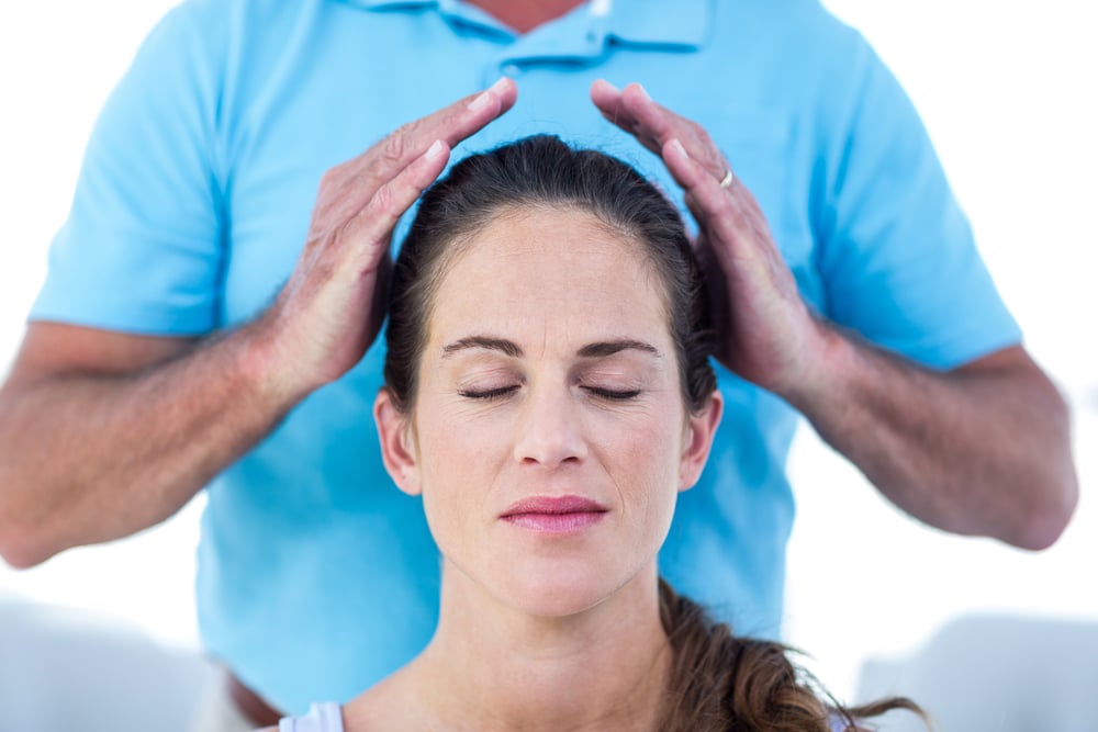 Therapist performing reiki on young woman at home